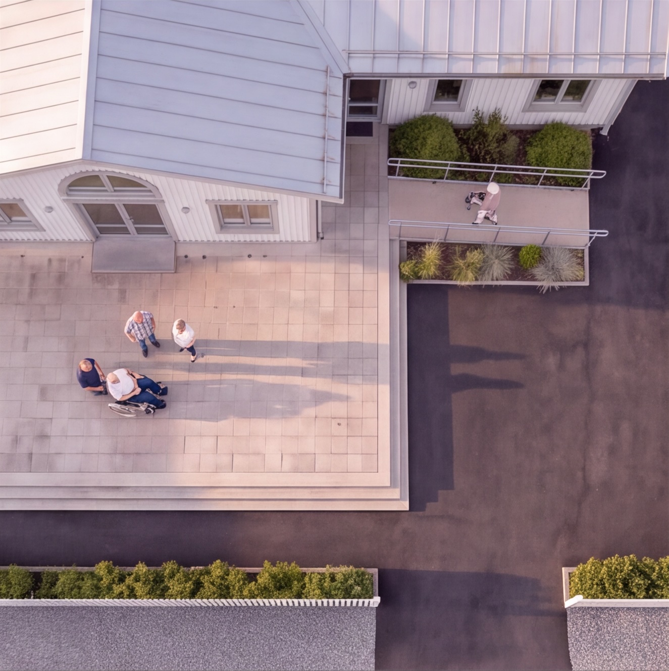 Flygfoto över entréplatsen vid ett Trygga Hus, där fyra personer samtalar och en boende går med rullator längs rampen